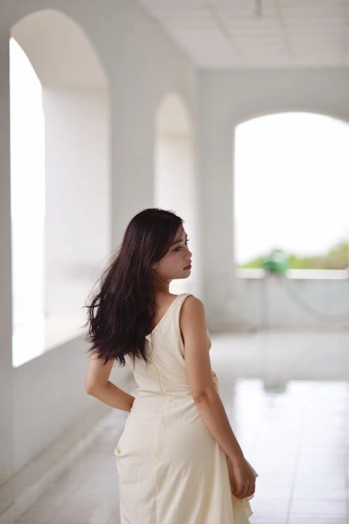 Miễn phí Góc nhìn nghiêng của một người phụ nữ thanh lịch trong chiếc váy trắng đang đứng ở hành lang hình vòm sáng sủa. Ảnh lưu trữ