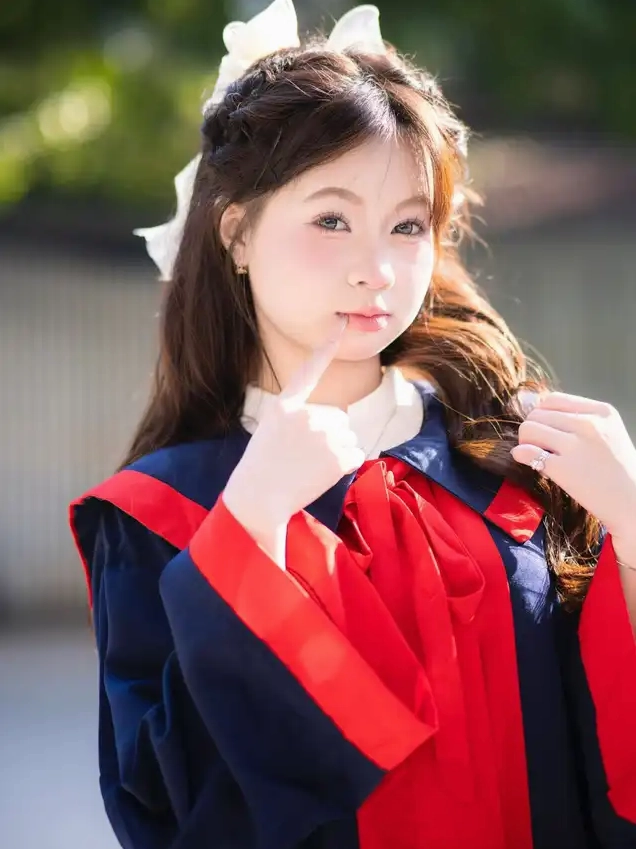 Cô gái trẻ trong trang phục cử nhân xanh đỏ nhìn thẳng vào ống kính với vẻ mặt trầm tư và đặt ngón tay lên môi