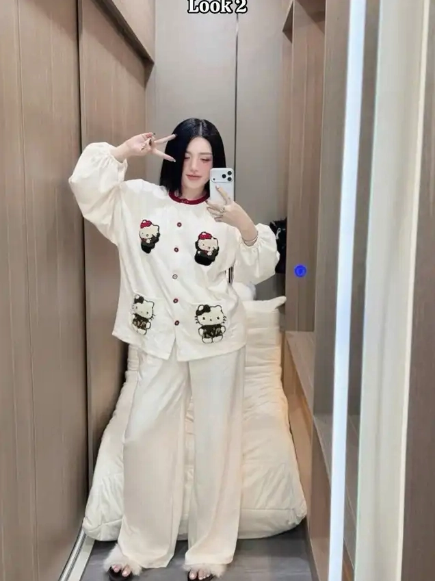 Một cô gái chụp ảnh selfie trong gương mặc bộ đồ ngủ màu kem in hình nhân vật hoạt hình mèo tạo dáng chữ V