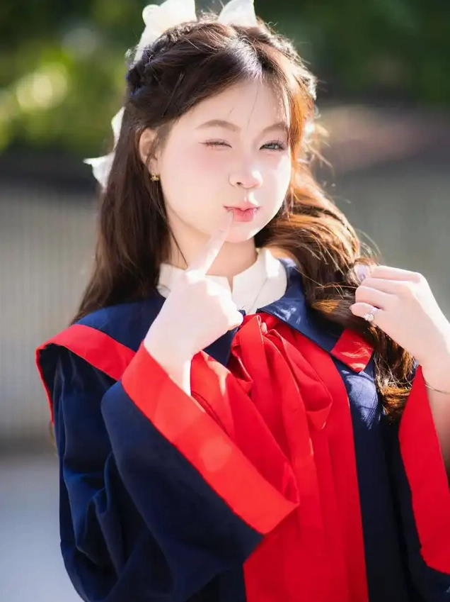 Một cô gái trẻ trong trang phục cử nhân xanh đỏ nháy mắt và đặt ngón tay lên môi tạo dáng đáng yêu